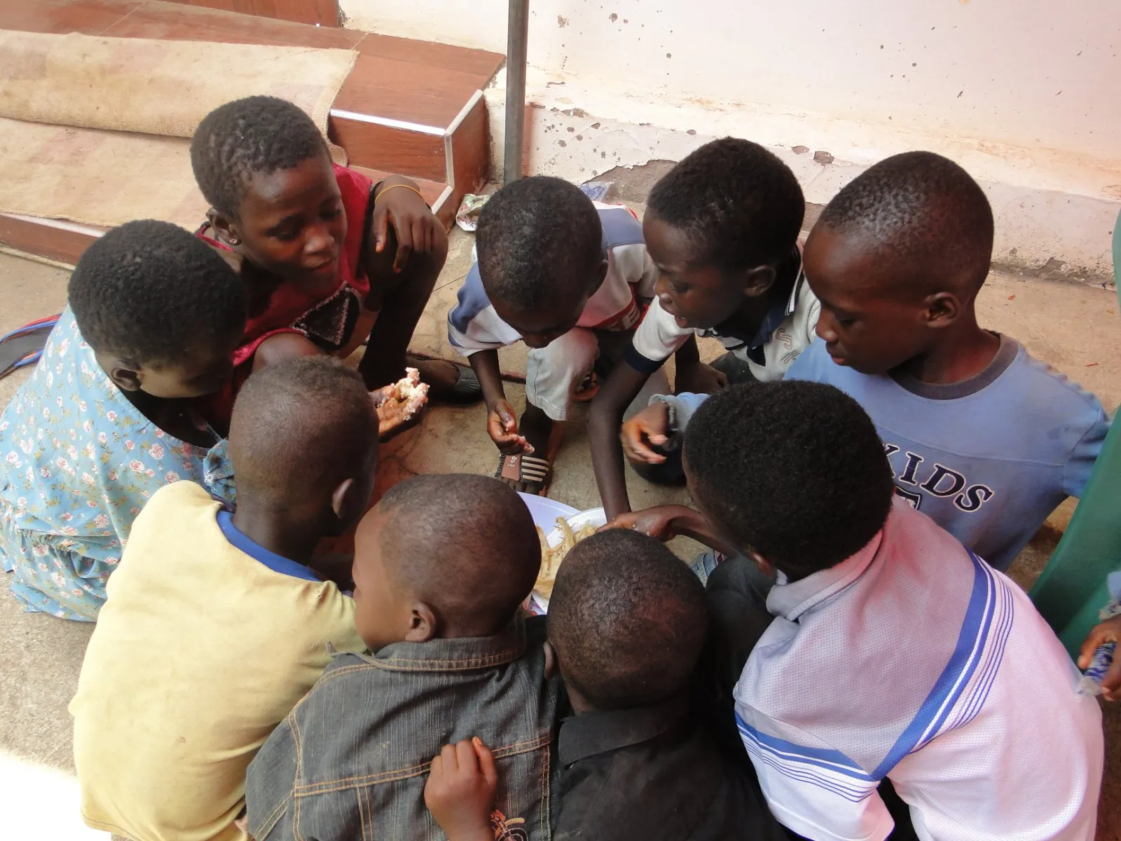 Children crouched together on a step, sharing a plate of food.