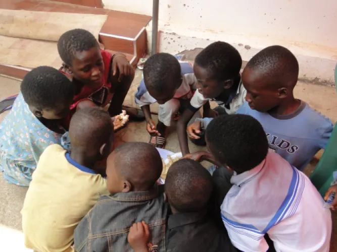 Children crouched together on a step, sharing a plate of food.